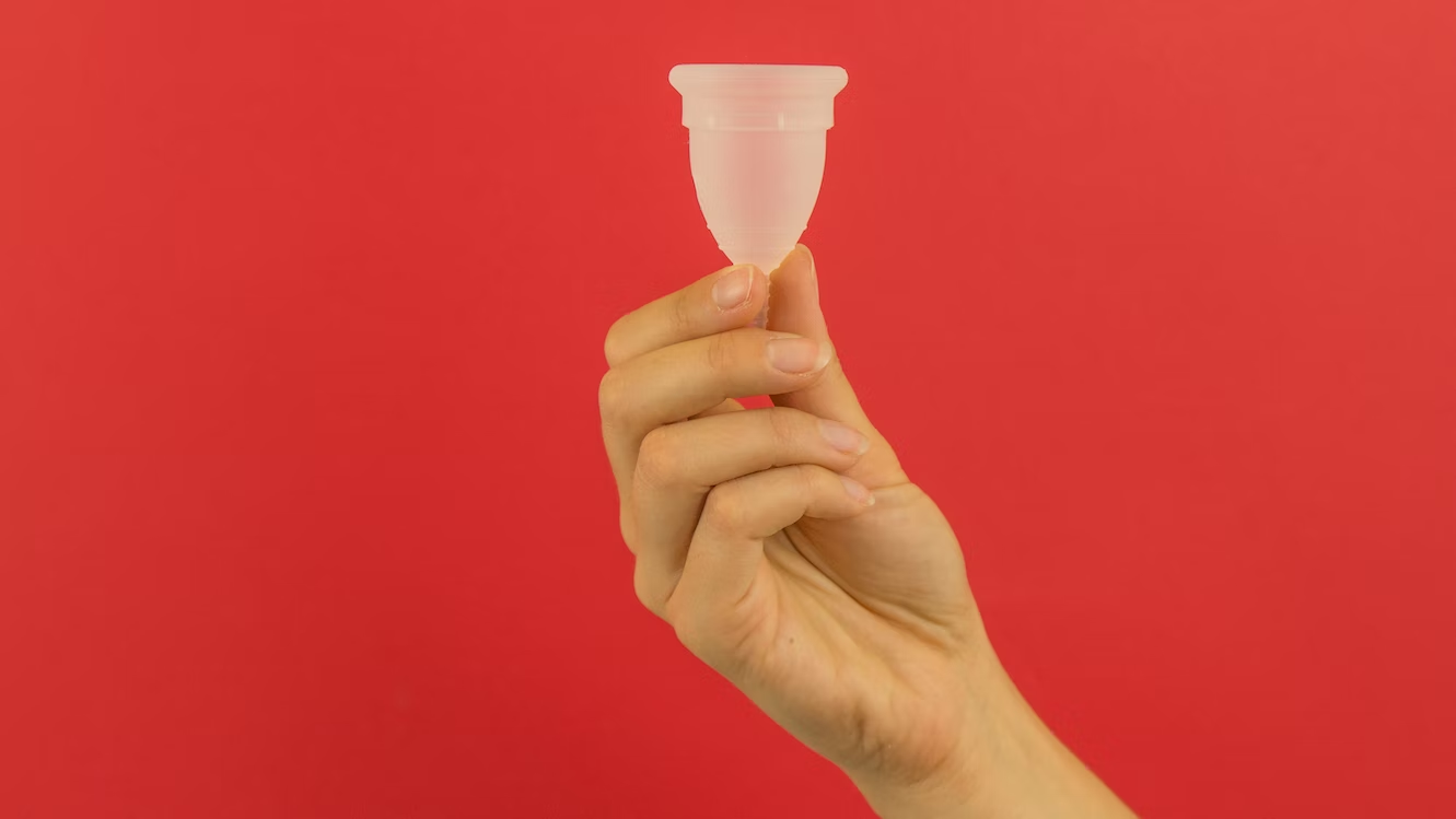 main tenant une cup menstruelle de couleur transparente sur fond rouge
