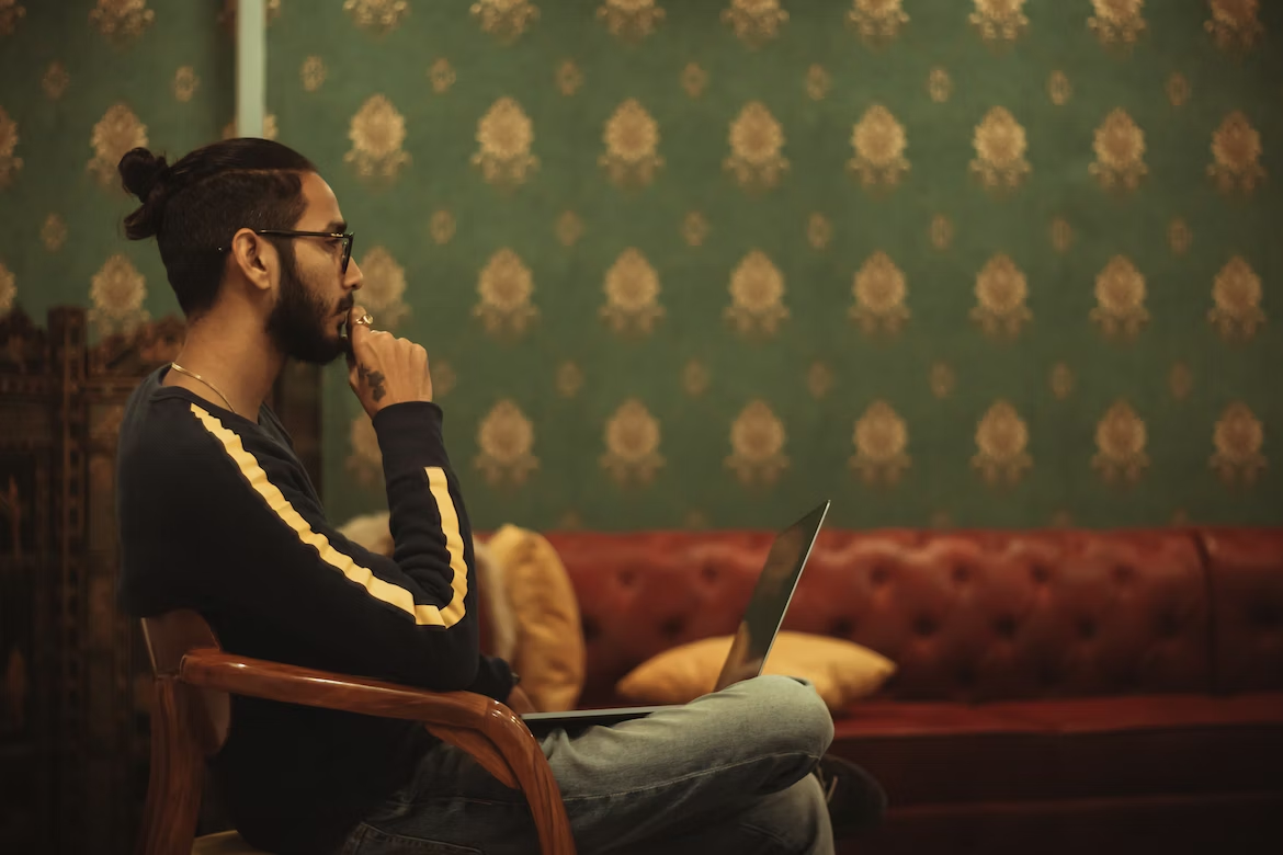 Homme de profil assis sur une chaise avec son ordinateur sur les genoux et réfléchissant