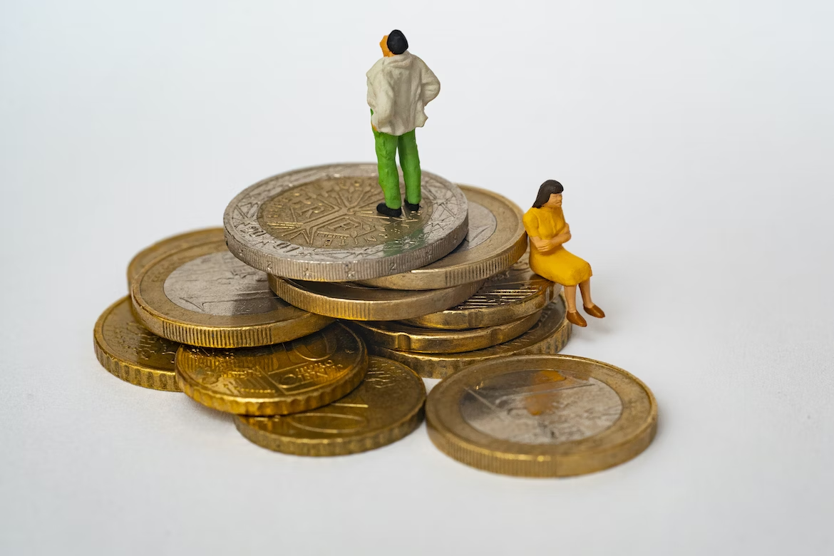 Deux figurines en céramique portant une veste beige, un pantalon vert et une robe jaune sont assises sur des pièces de monnaie