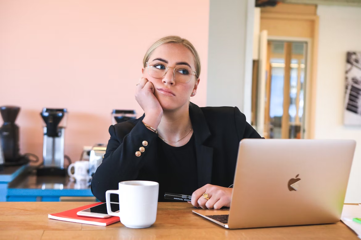 Femme blonde avec des lunettes réfléchissant devant son ordinateur Macbook Air rose