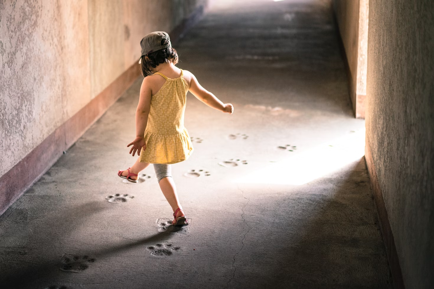 Petite fille portant une robe jaune marchant dans un couloir et suivant des traces de pattes d'animal