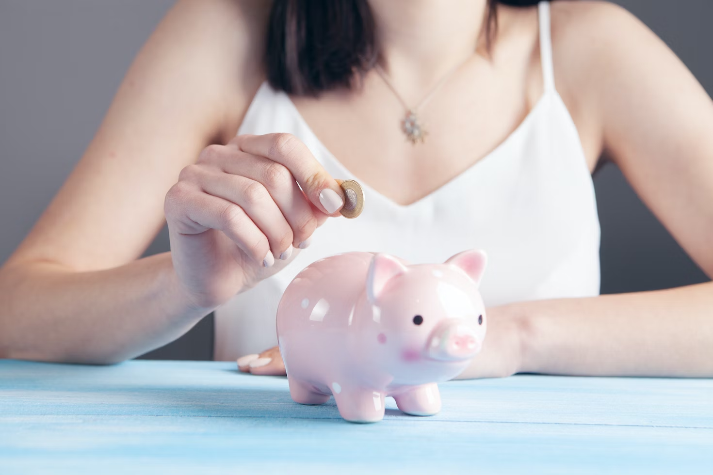 Femme en débardeur blanc mettant une pièce de monnaie dans une tirelire en forme de cochon rose