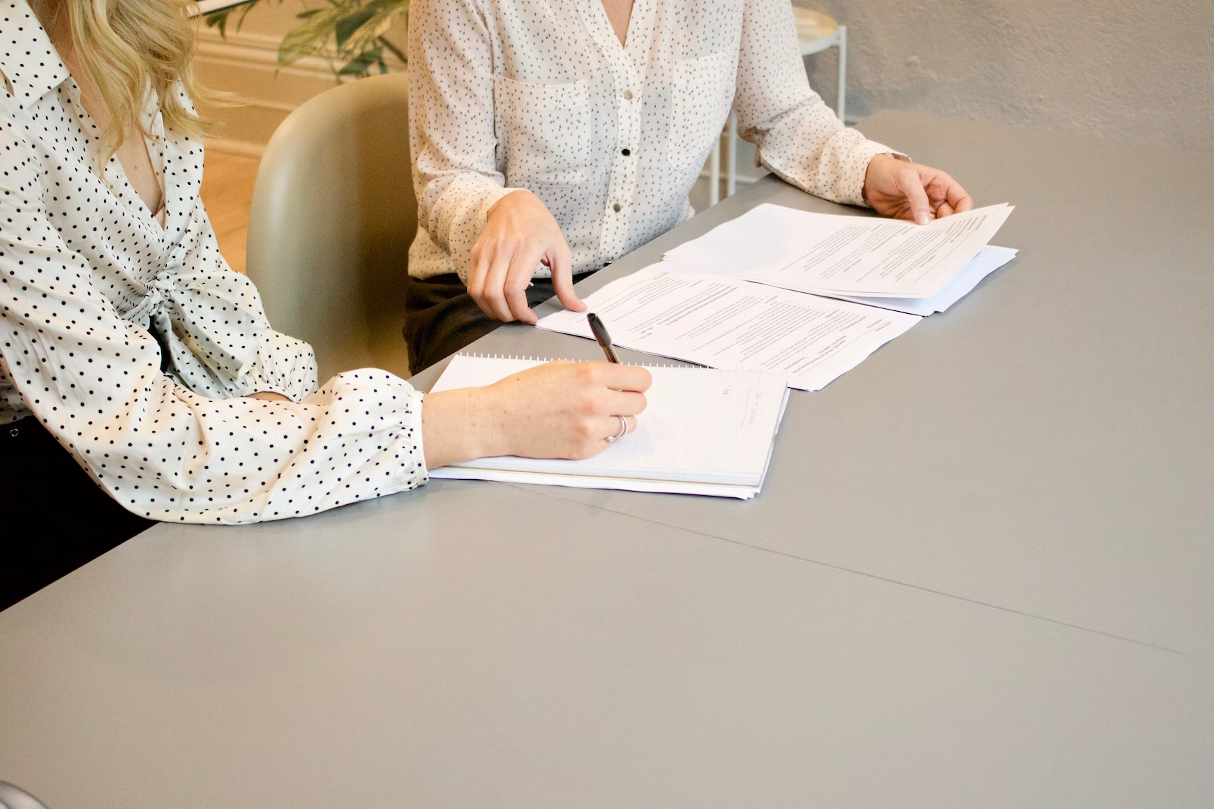 Une femme avec une chemise à pois tenant un stylo et écrivant sur un carnet et une autre femme tenant des documents