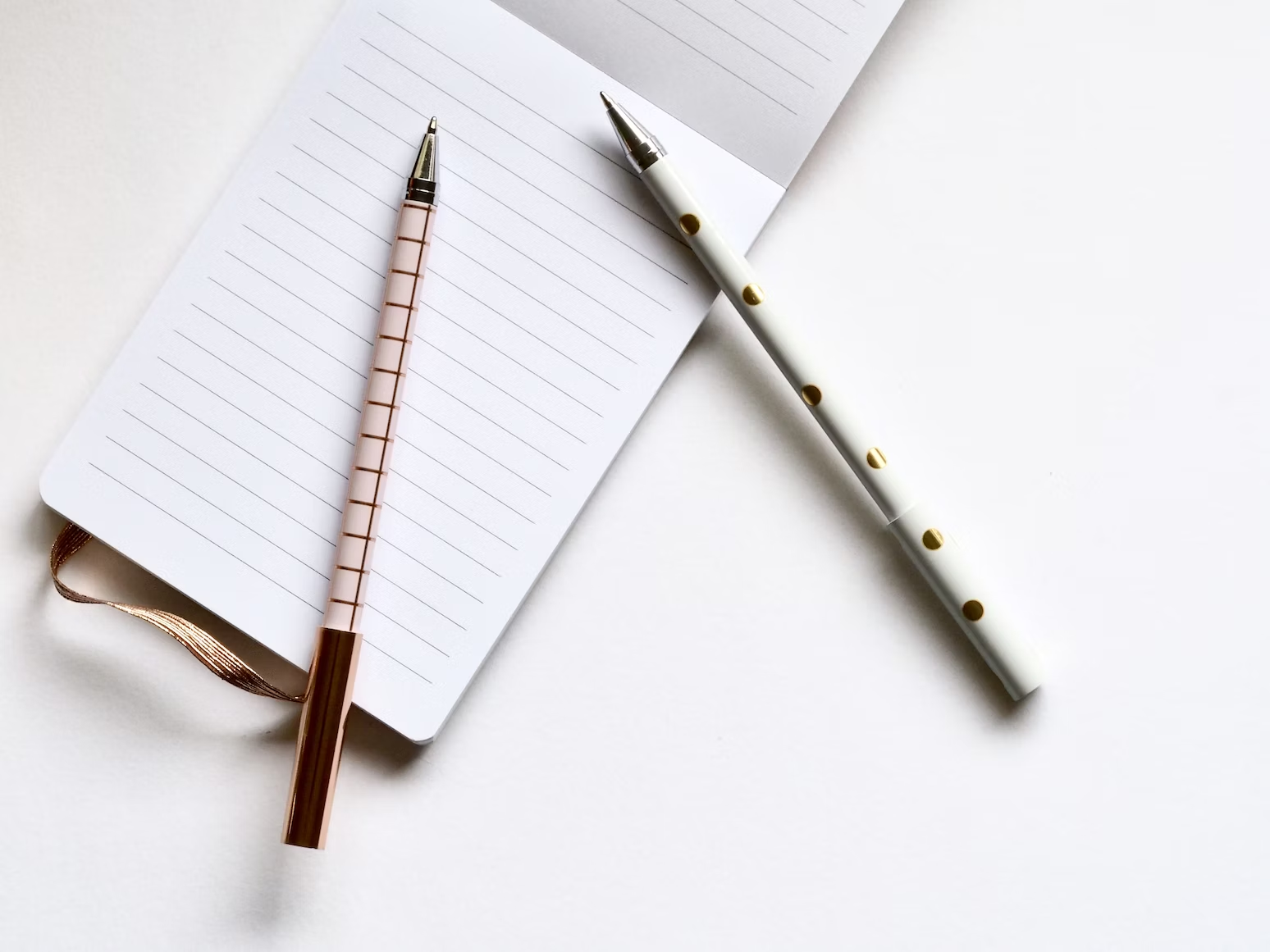 Deux stylos blancs à carreaux et à pois reposant sur un calepin ouvert sur une table blanche
