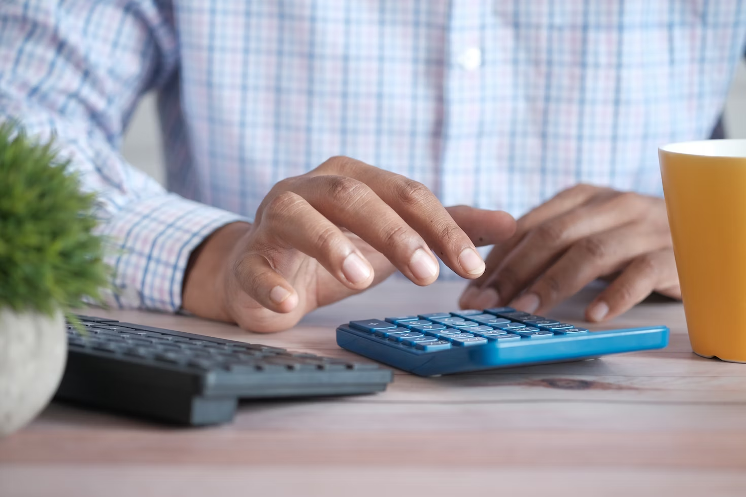 Homme portant une chemise à carreaux blancs, bleux et roses et tapant sur une calculatrice bleue.