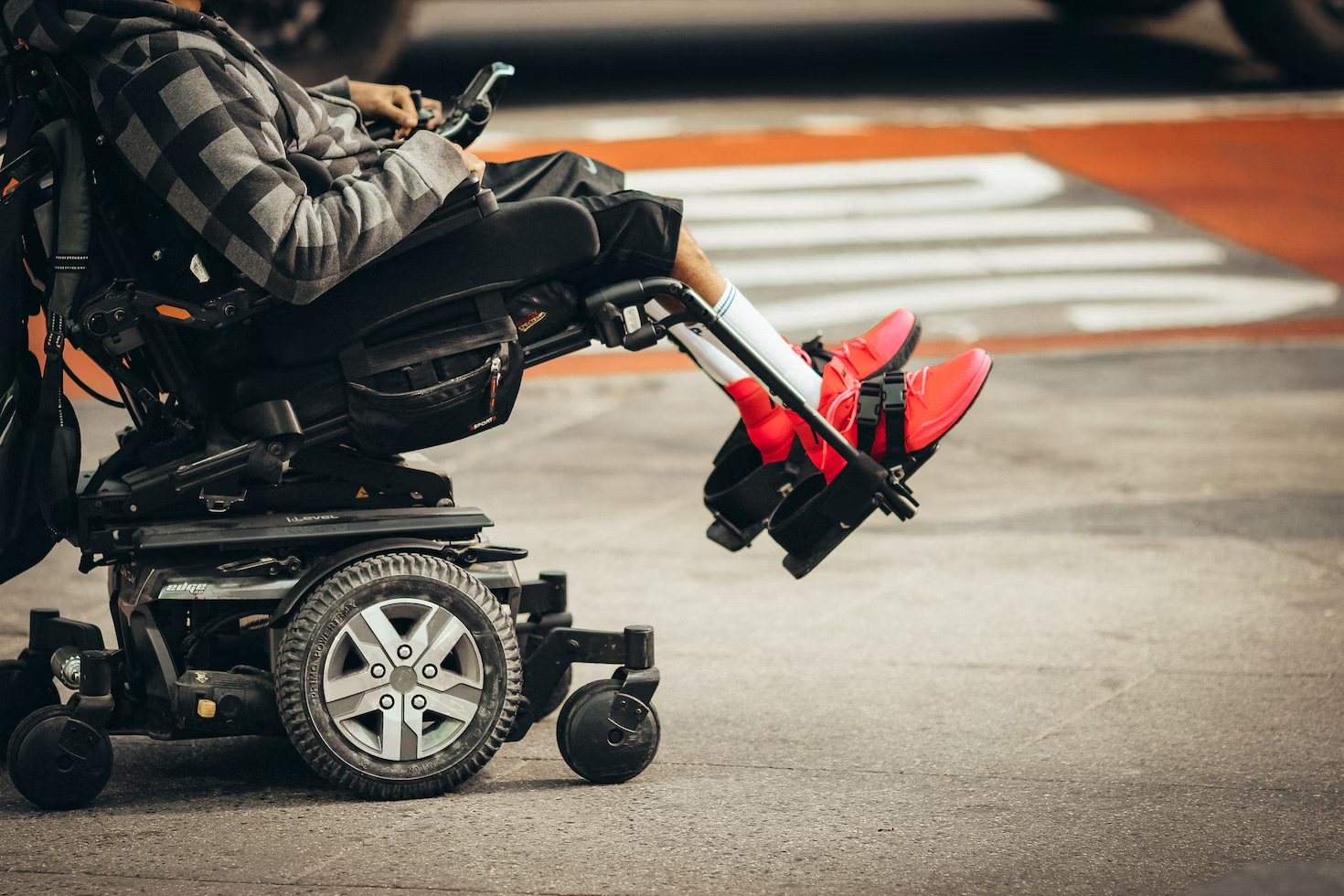 homme en veste à carreaux et en pantalon noir avec des baskets rouges conduisant un fauteuil roulant.