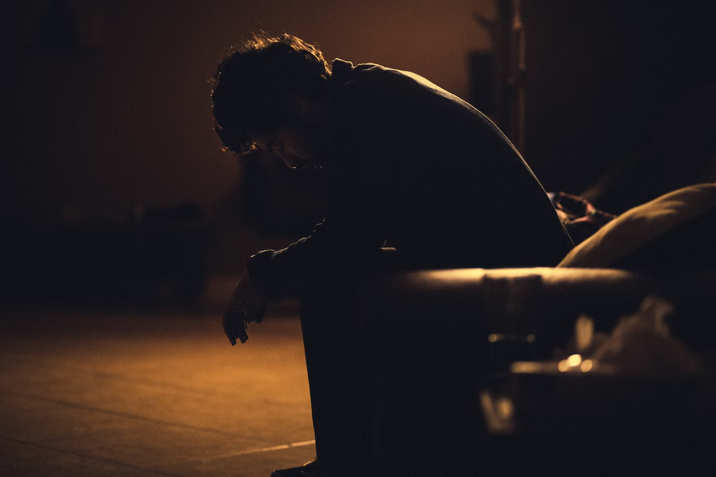 Homme se tenant assis les épaules voûtées et les bras croisés regardant le sol dans le noir