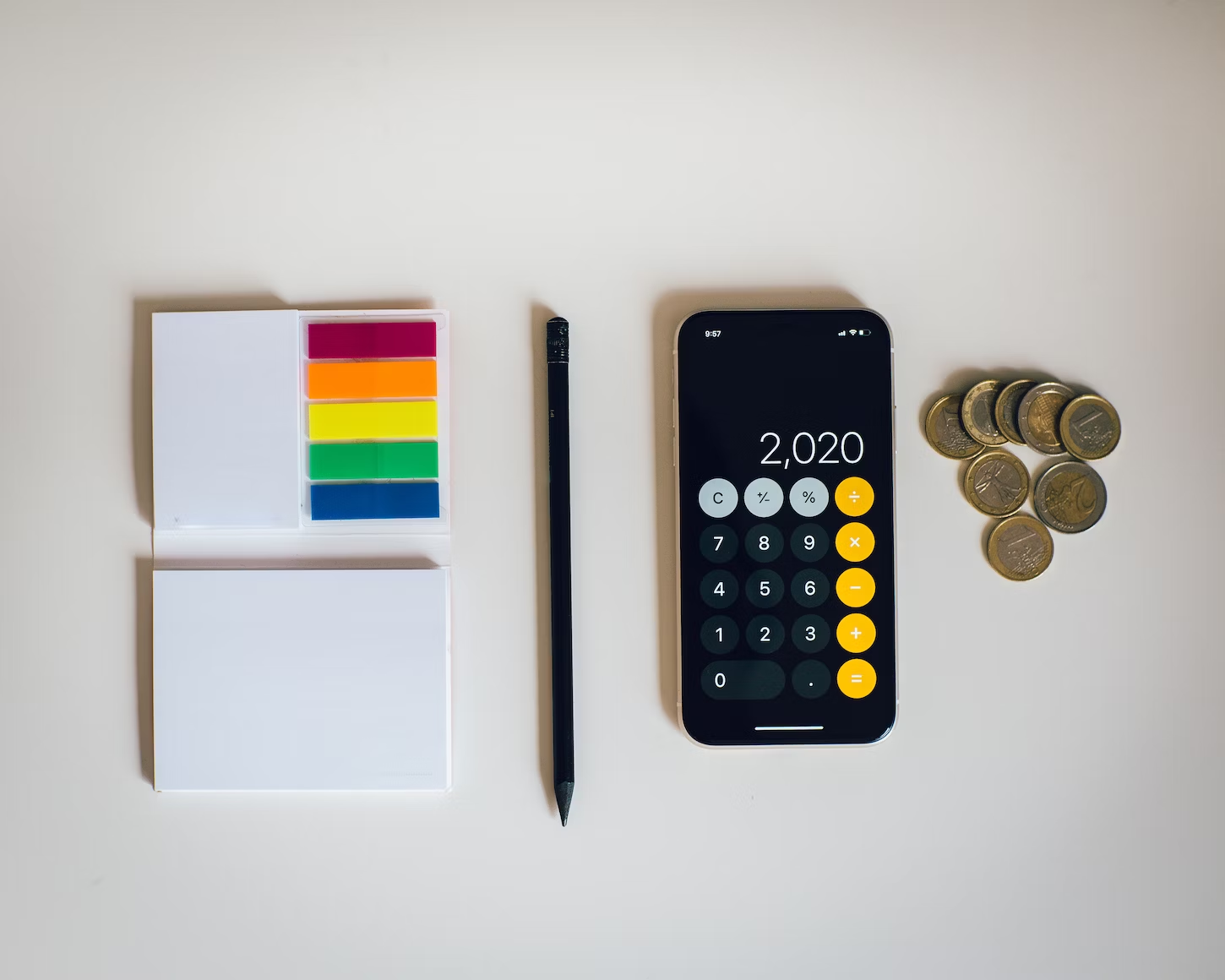 IPhone avec l'application calculatrice posé à côté de post-its de couleur, d'un crayon à papier et de pièces