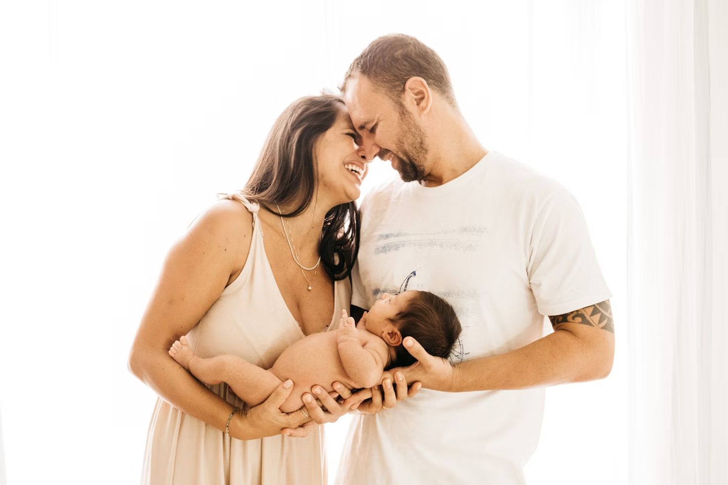 Homme en T-shirt blanc et femme en robe blanche tenant un bébé dans ses bras qui s'embrassent