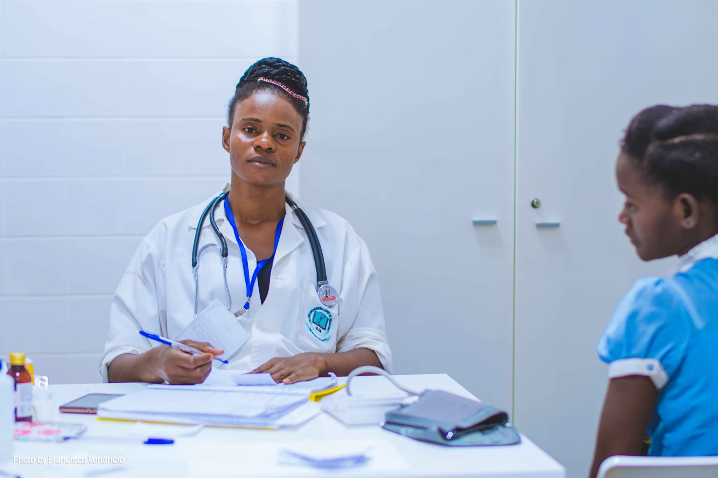 Femme médecin portant un sthétoscope autour du cou écrivant sur des papiers à côté de sa patiente portant une robe bleue