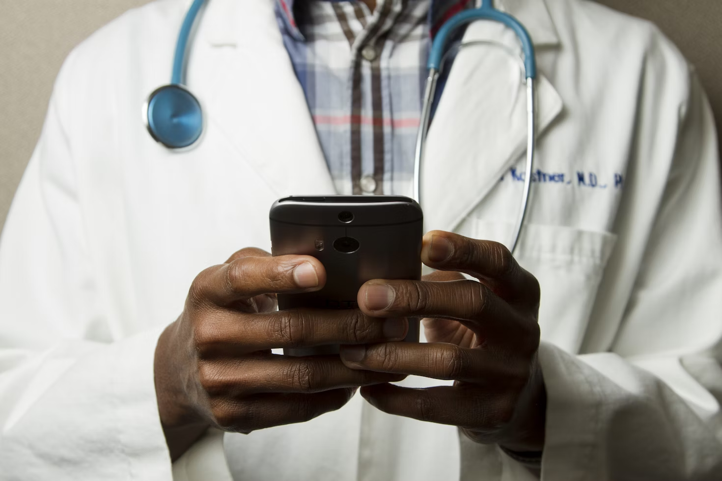 Médecin en blouse blanche avec un stéthoscope autour du cou écrivant sur son téléphone portable