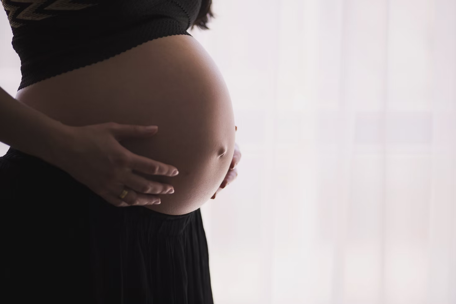 Femme enceinte tenant son ventre avec ses deux mains et portant un haut et un pantalon noirs