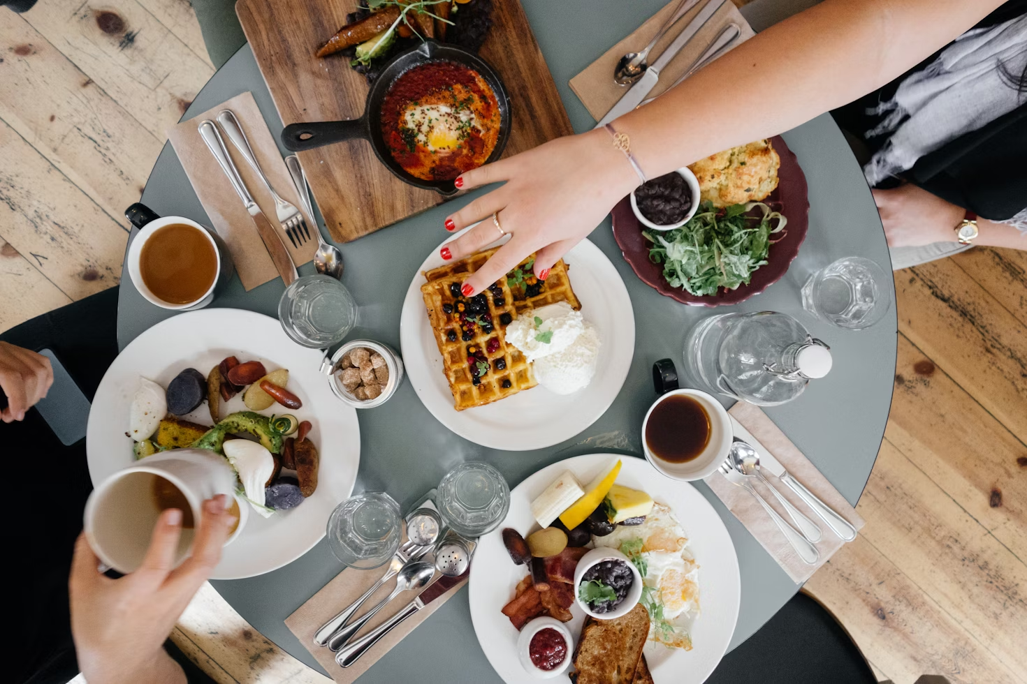 Variété d'aliments posés sur une table ronde et grise avec plusieurs personne tendant leur main pour attraper quelque chose