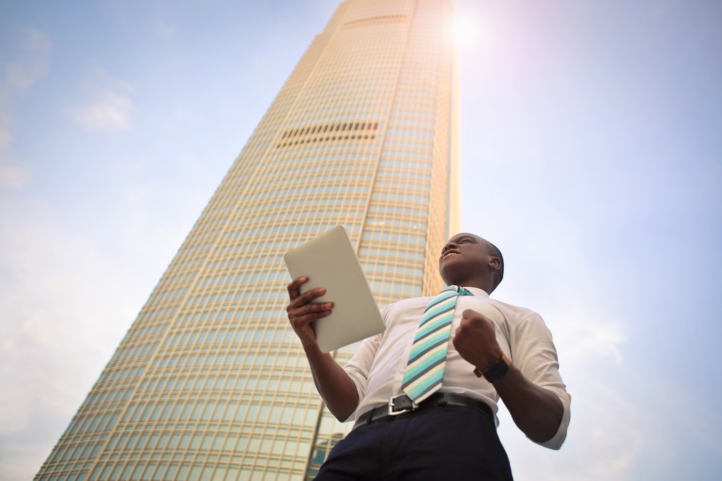 Homme avec une chemise blanche et une cravate rayée bleue grise et jaune tenant un document devant un gratte-ciel
