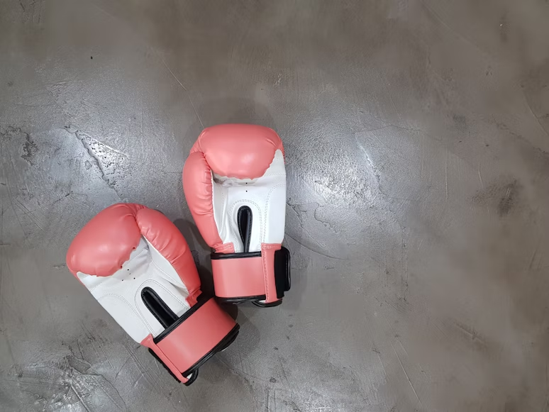 Deux gants de boxe roses et blancs posés sur un sol en béton ciré gris