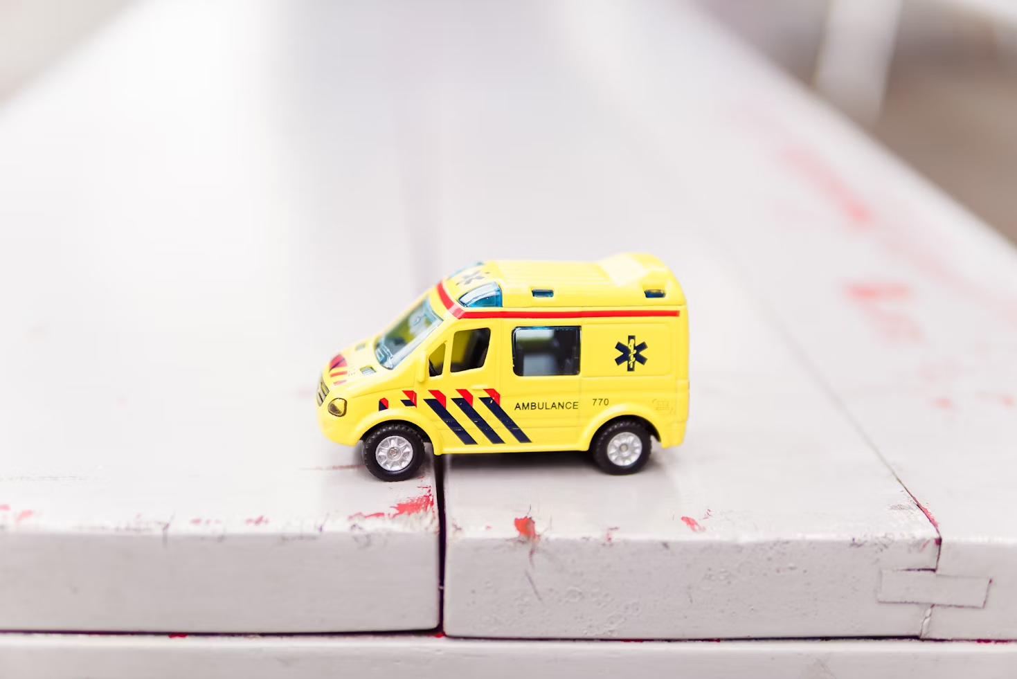 Jouet représentant un camion d'ambulance jaune avec des rayures bleues marines et rouges