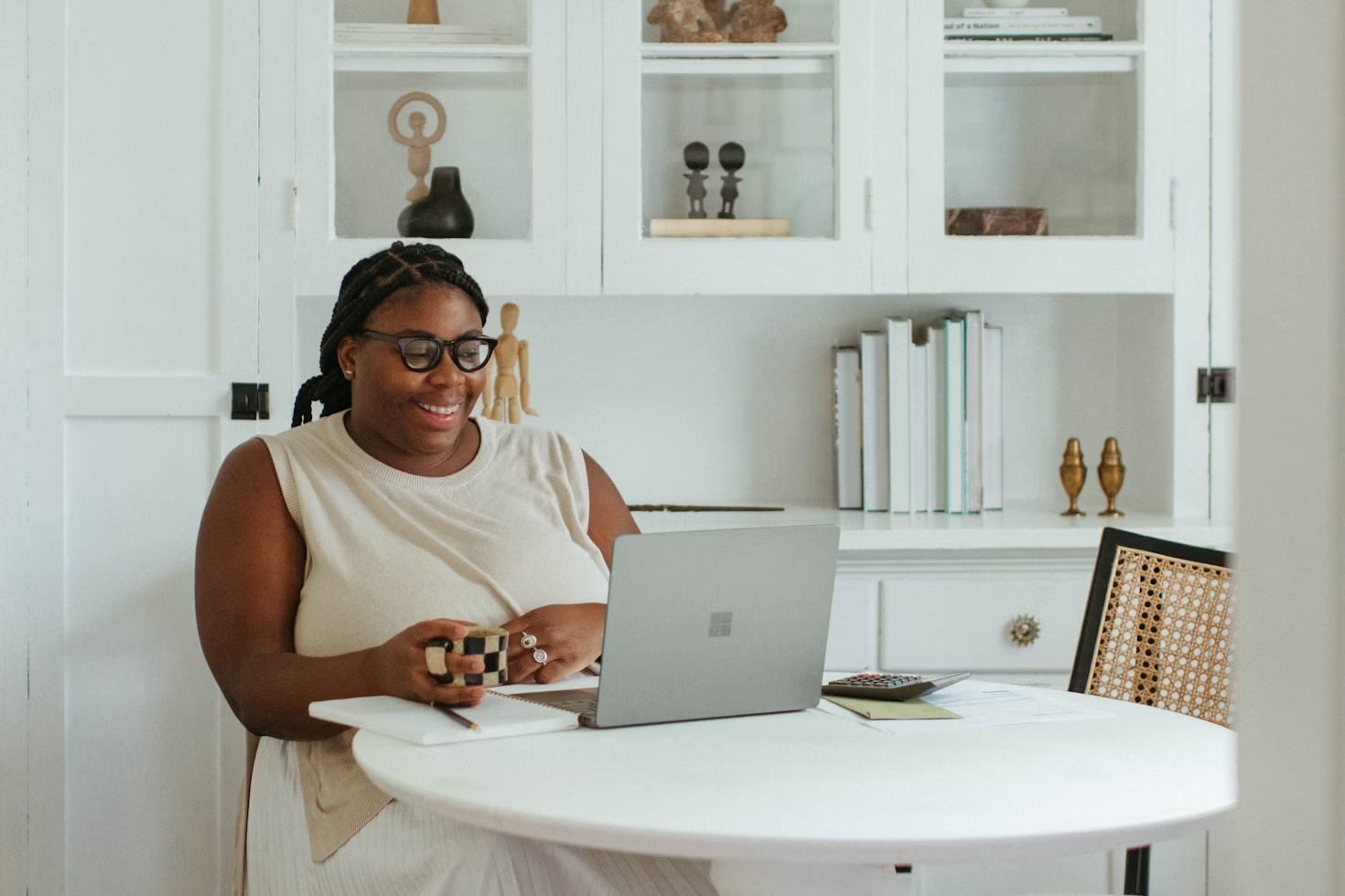 Femme portant des lunettes un haut et une jupe blancs tenant un mug à damiers blancs et noirs travaillant sur son ordinateur