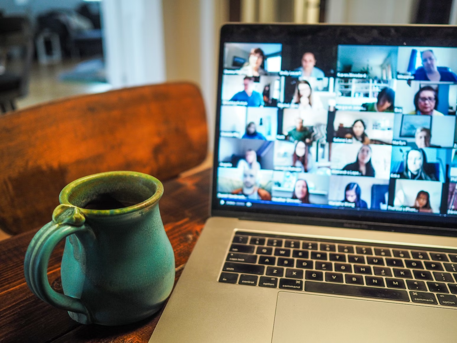 Macbook Pro posé sur une table à côté d'un mug bleu montrant des gens connectés sur Zoom via une webcam