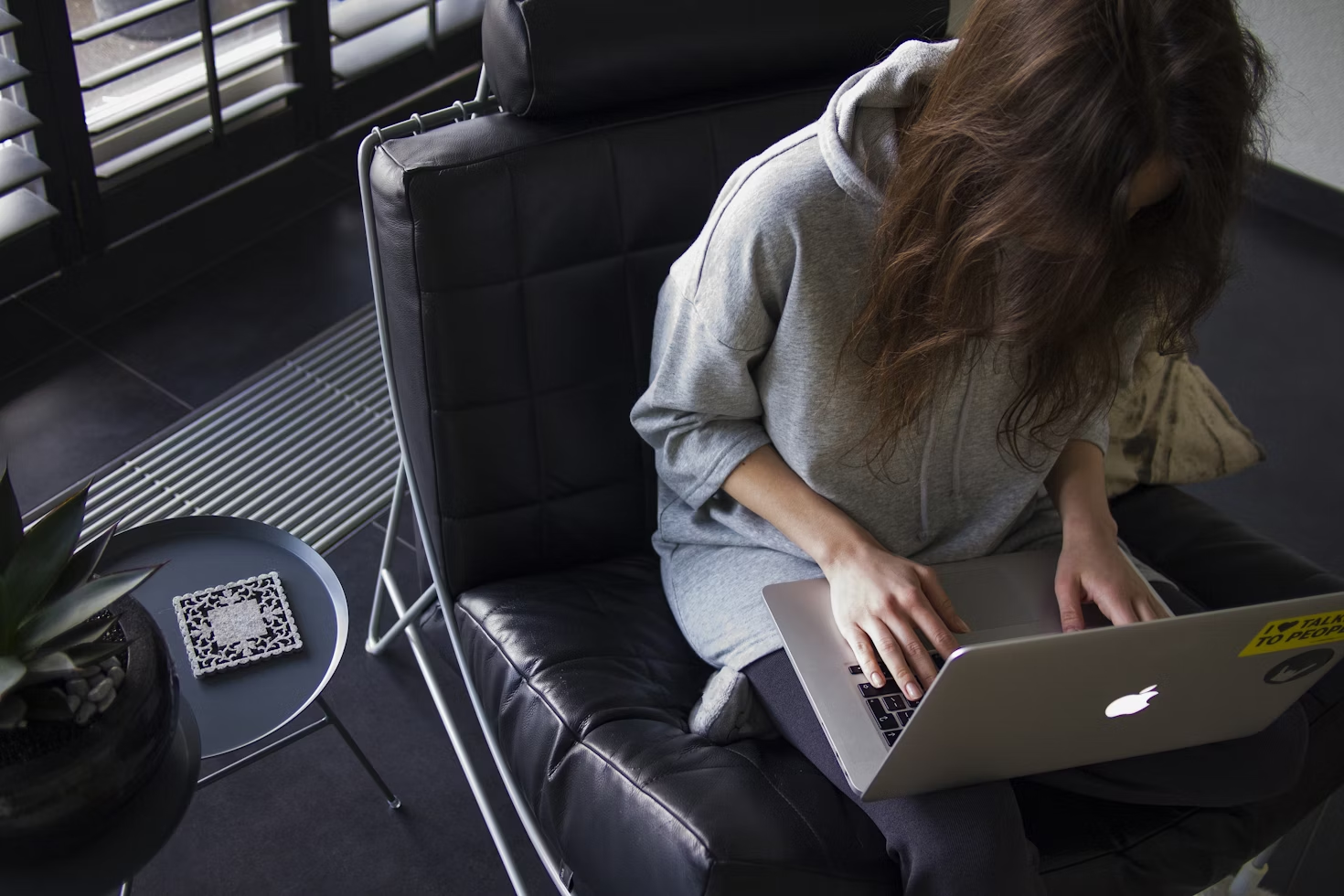Femme en sweatshirt gris à manches longues assise sur un fauteuil matelassé noir et tapant sur son Macbook
