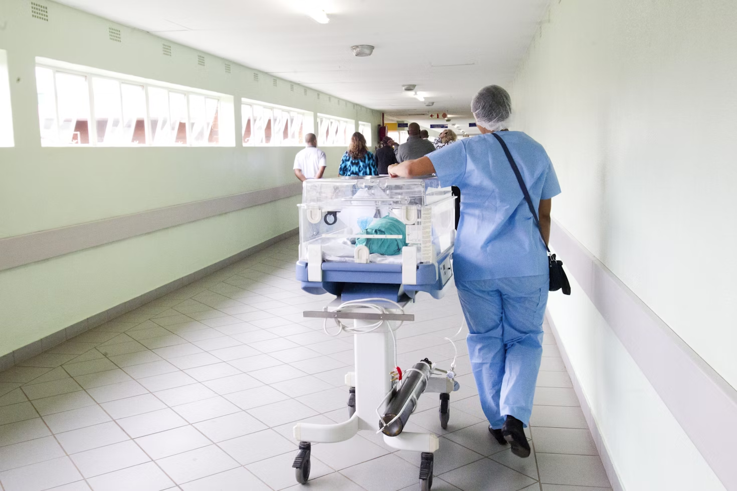 Personne en uniforme de médecin et portant une charlotte marchant dans le couloir à côté de l'incubateur