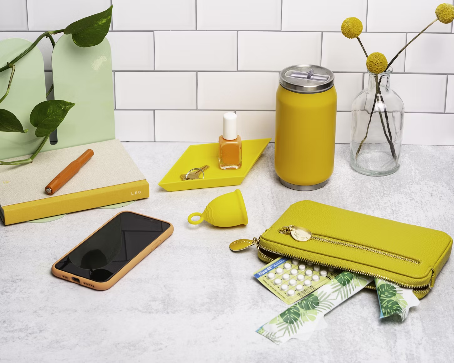 Trousse avec des tampons et la pilule posée sur un bureau à côté d'une cup menstruelle d'un téléphone et d'une gourde jaune