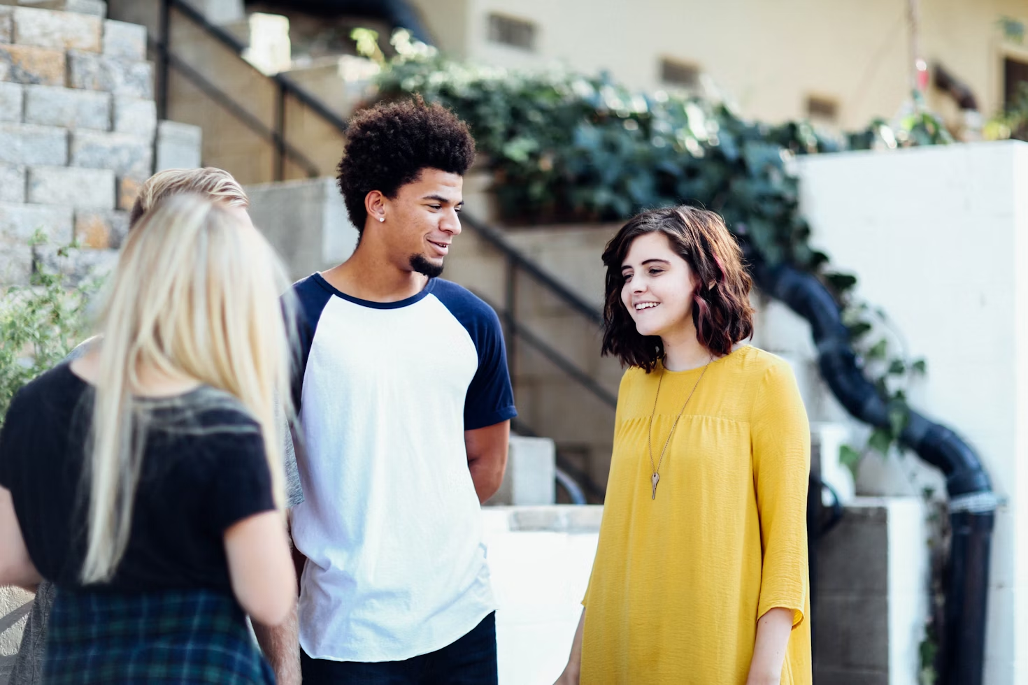 Quatre personnes parlant ensemble à l'extérieur avec un homme en T-shirt blanc et bleu regardant une femme brune avec un T-shirt jaune