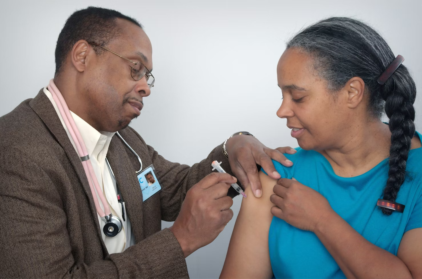 Médecin portant un blazer marron à rayures faisant une piqure dans l'épaule d'une patiente avec une seringue