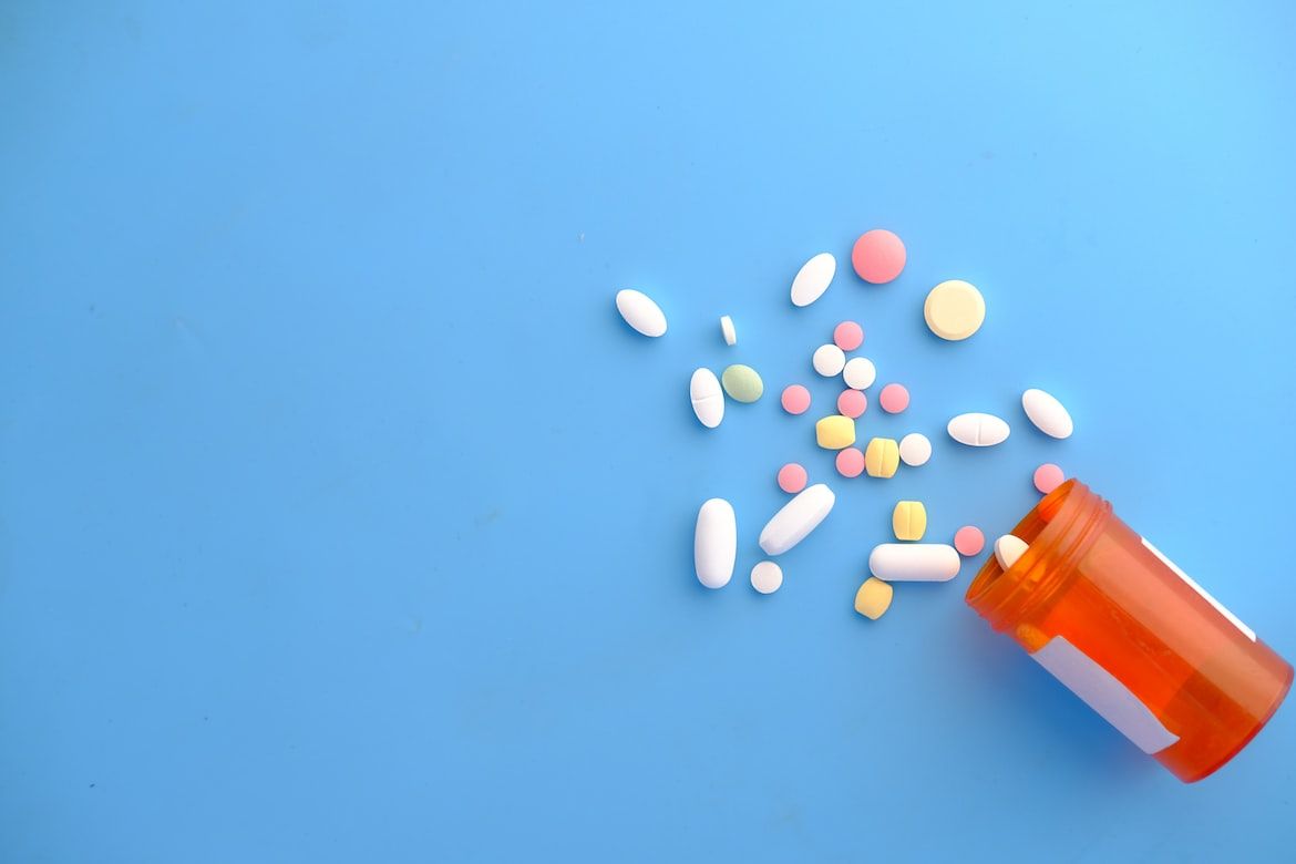 boite de médicaments cylindrique avec des comprimés éparpillés de couleur blanche, jaune, verte et rose sur fond bleu